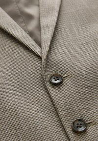 Blazer à motif pied-de-poule beige et marron avec deux boutons foncés et un col à revers visible.