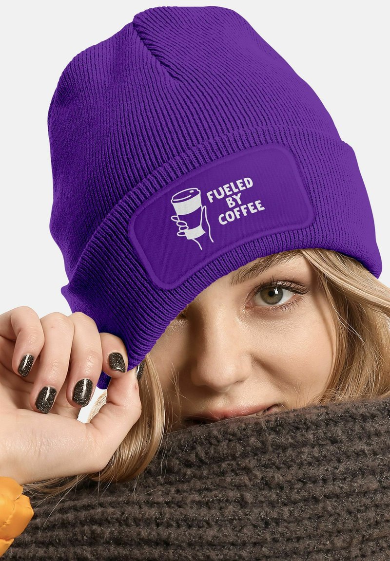 Purple knitted beanie with a patch featuring the text "FUELED BY COFFEE" and a graphic of a coffee cup. Smooth texture, form-fitting design.