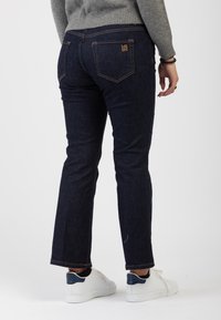 Jeans in denim scuro con un design a gamba dritta, caratterizzati da cuciture arancioni e tasche posteriori. Abbinati a sneakers bianche.
