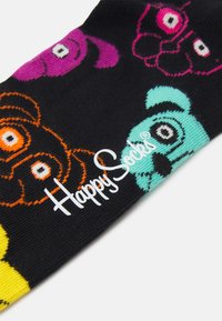 Barvite nogavice z črnim materialom in risanimi živalmi v vijolični, oranžni in teal barvi. Logotip "Happy Socks" je bel in se nahaja na strani.
