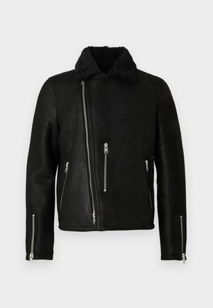 Chaqueta de cuero negra de estilo motero con cremallera frontal asimétrica, tres bolsillos con cremallera, cremalleras en los puños de las mangas y un suave collar de forro polar.