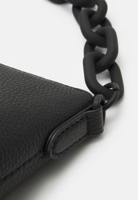 Svart läderväska med en texturerad yta, vinkelräfflad form och stor matt kedjestraps för bärande.