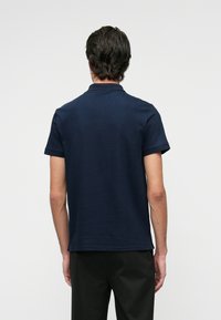 Sötétkék pólóing, gallérral, rövid ujjal és egyenes szegéllyel. Simaság jellemzi, látható logók vagy minták nélkül.