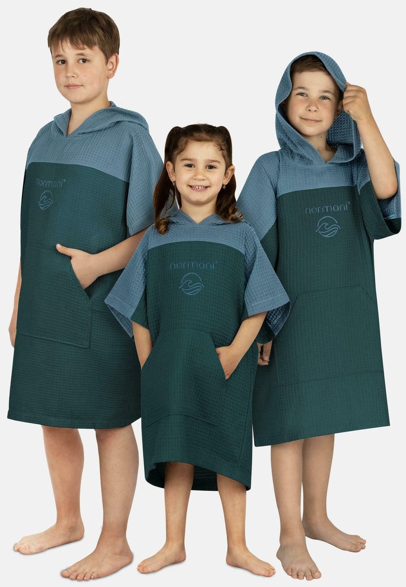 Hooded Bad Ponchos aus blauer und grüner Waffelware mit einer Fronttasche und einem Logo, getragen von drei Kindern unterschiedlicher Größen.