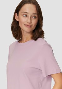 Jasnolawendowa koszulka z krótkim rękawem, wykonana z miękkiego materiału, z okrągłym dekoltem i luźnym krojem. Prosty design bez widocznych wzorów.