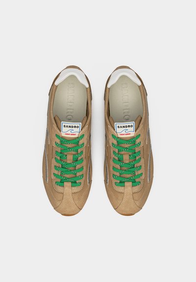 Ζευγάρι μπεζ σουέντ αθλητικά παπούτσια με πράσινα κορδόνια, λευκές λεπτομέρειες στη φτέρνα και ετικέτα «Sandro Light Wave» στη γλώσσα, φαίνεται από πάνω.