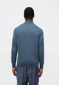 Polo de manga comprida para homem em tecido de malha azul suave. Apresenta uma gola plana, punhos e bainha canelados, com um design de corte justo.