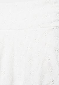 Tissu blanc avec motif floral ajouré brodé en diagonale et détail de couture froncée.