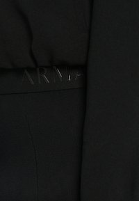 Musta aktiivivaatetus, joka sisältää tiukan topin ja legginsit. Vyötärönauhas on kohokuvioitu "ARMANI" -brändäys, ja siinä on sileä, joustava rakenne.