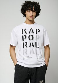 T-shirt en coton blanc avec des lettres noires audacieuses et des coordonnées. Coupe standard, manches courtes et col rond. Shorts noirs avec un accent de logo.
