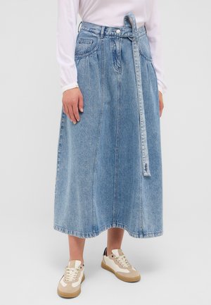 Jeansrock, hellblau, knielang mit einem Gürtelbund, ausgestattet mit zwei Seitentaschen und sichtbaren Nähmustern. Kombiniert mit beigen Sneakers.