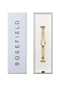 Montre-bracelet en mailles dorées avec un cadran blanc rectangulaire, présentée dans une boîte blanche affichant le nom de la marque "ROSEFIELD."