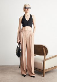 Svart avkortet halter-top, beige vide bukser med folder, spisse svarte hæler, og en liten svart veske på en lys bakgrunn.