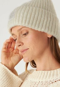 Crème ribgebreide beanie met een geweven logo patch. De textuurstof en het slouch-design passen goed bij een off-white gebreide trui.
