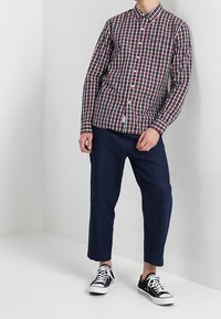 Chemise boutonnée avec un motif à carreaux rouge et marine, associée à un pantalon court marine foncé et des baskets noires et blanches.