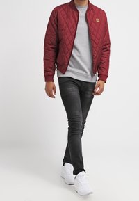 Bordo prošívaná bomber bunda, šedá mikina, černé džíny a bílé tenisky. Výrazný diamantový vzor na bundě; žebrované manžety.