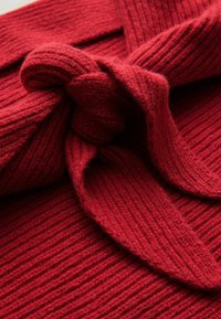 Tissu en tricot rouge avec une texture côtelée, présentant un design noué. Le matériau semble doux et épais, adapté pour la chaleur.