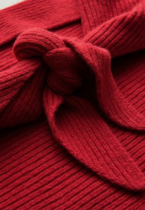 Tessuto lavorato a maglia rosso con una texture a coste, caratterizzato da un design annodato. Il materiale sembra morbido e spesso, adatto per il caldo.