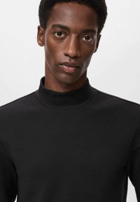 Crna mašna s visokim ovratnikom, prilagođenog dizajna i glatke teksture, s minimalnim šavovima na ramenima.