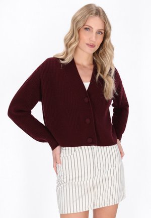 Burgundy neulecardigan, jossa on syvä V-pääntie ja kolme pyöreää nappia, pitkät hihat ja lyhyt leikkaus. Yhdistetty raidoitettuihin hameisiin.