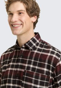 Czarna i czerwona koszula flanelowa w kratę, z kołnierzykiem zapinanym na guziki, wyposażona w jedną kieszeń na piersi oraz wykonana z miękkiego, teksturowanego materiału.