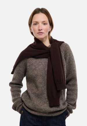 Pull en laine marron à manches longues, présentant un tricot texturé. Une écharpe marron foncé est drapée sur les épaules.