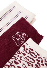 Tres pares de calcetines: uno crema con rayas marrón, uno marrón con un diamante bordado y corazones, y uno crema con un patrón de leopardo.