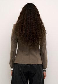 Braune taillierte Jacke mit langen Ärmeln und weißen gestreiften Bündchen, kombiniert mit schwarzen Lederhosen. Das Material wirkt glatt mit subtiler Textur.