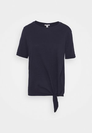 Camiseta de manga corta azul marino con cuello redondo y detalle anudado en la parte inferior izquierda. Tela suave y texturizada con mangas remangadas.