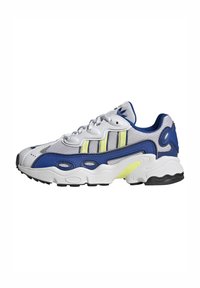 Baskets de sport en blanc, bleu et jaune. Dessus en maille et synthétique avec un design incurvé, un laçage prononcé et une semelle texturée avec des accents.