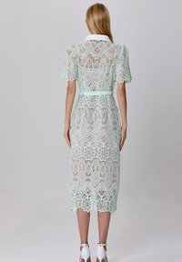 Robe en dentelle vert menthe avec des manches courtes, un col et une taille ceinturée. Le design présente un motif floral et une longueur midi.