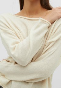 Helles, cremfarbenes Strickoberteil mit einem lockeren, schulterfreien Design. Verfügt über gerippte Bündchen und eine entspannte Passform, die einen weichen, strukturierten Stoff zeigt.