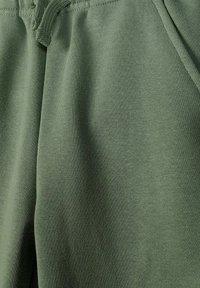 Gros plan sur un short en tissu vert olive avec une texture visible et un cordon tressé à la taille.