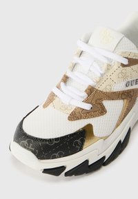 Sneaker alb cu accente aurii și maronii, texturi combinate inclusiv plasă și piele, având o vârf neagră și detalii proeminente cu logo.