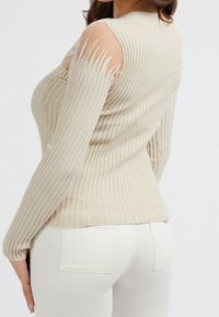 Béžový žebrovaný svetr s dlouhým rukávem, s průhlednými síťovanými panely na ramenou a jemnými třpytivými nitěmi. Přiléhavý střih s kulatým výstřihem.