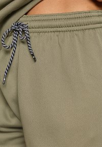 Shorts de sport vert olive en tissu maillé respirant, dotés d'un cordon de serrage noir et blanc avec embouts en métal et d'une taille élastique.