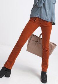 Pantalones skinny de color óxido, confeccionados en una mezcla de algodón, con un diseño clásico de cinco bolsillos, combinados con una camisa azul clara y botas de plataforma negras.