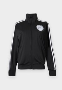 Schwarze Trainingsjacke mit Reißverschluss, weißen Streifen an den Ärmeln und einem grauen Adidas-Trefoil-Logo mit Rüschendetail auf der Brust.