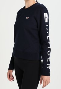 Felpa blu navy con collo a giro, polsini a costine e un piccolo logo sul petto, accompagnato da una scritta bianca audace lungo la manica.