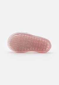 Suela de zapato translúcida de color rosa con una superficie texturizada y purpurina plateada incrustada, que presenta una forma redondeada y una ligera curva en el talón.