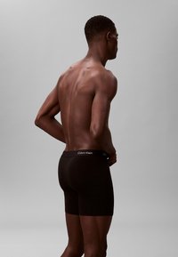 Czarne bawełniane slipy w formie bokserów o dopasowanym kroju, z elastycznym paskiem z marką. Model pokazany jest z boku, co podkreśla design.