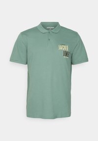 Polo a maniche corte di colore verde tenue, realizzato in cotone. Presenta un colletto e una piccola grafica sul petto con "JACK & JONES" in giallo e nero.