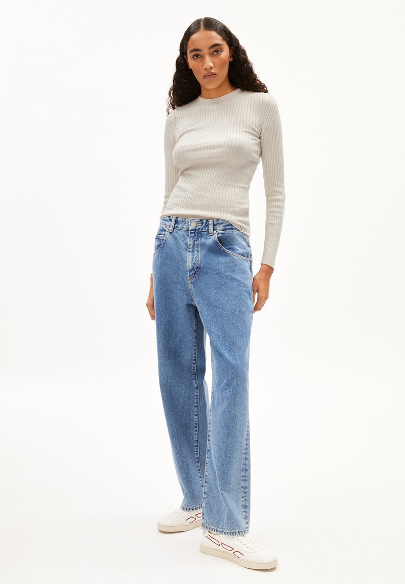 Hellgraues, gerippte Langarmoberteil, kombiniert mit hochtaillierten, lockeren blauen Jeans aus Denim. Weiße Sneakers mit roten Akzenten runden den Look ab.