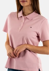 Polo rosa chiaro con collo con risvolto, maniche corte e una patta frontale con bottoni. Dettaglio logo sul petto a sinistra.