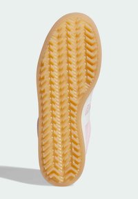 Semelle d'une basket présentant un motif en chevrons texturé en caoutchouc marron, avec une tige rose et des accents blancs sur les côtés.