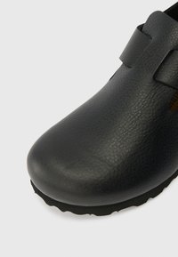 Zwarteleren schoen met een ronde neus, gestructureerd oppervlak en een band over de bovenkant. Beschikt over een flexibele rubberen zool met een gestructureerde rand.