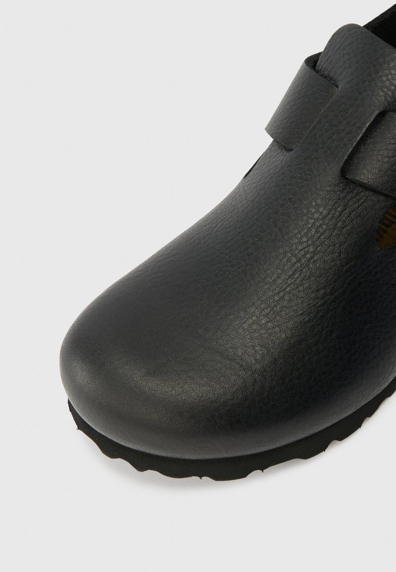 Schwarze Lederhose mit einer runden Zehenpartie, strukturierter Oberfläche und einem Riemen über dem Obermaterial. Verfügt über eine flexible Gummisohle mit einem strukturierten Rand.