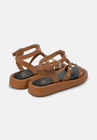 Bruine platte sandalen met verstelbare banden, gouden studs en een stevige zool. Gelaagd voetbed met een logo. Platformontwerp voor extra hoogte.