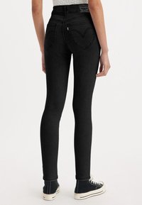 Jean skinny noir avec taille haute, poches arrière en forme de cœur et denim texturé ; associé à des baskets montantes noires.