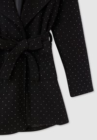 Czarny płaszcz z paskiem w talii, pokryty małymi białymi kropkami, z długimi rękawami i kołnierzem szalowym.